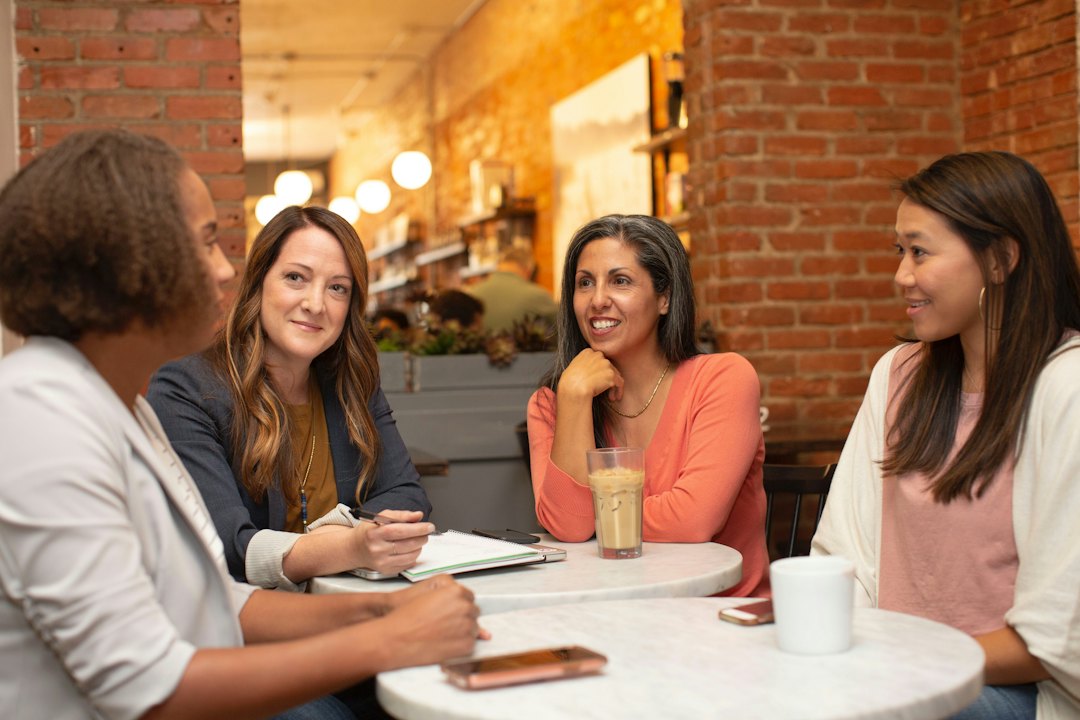 Vier Frauen sitzen im Gespräch an einem Tisch in einem Café und hören einander aufmerksam zu